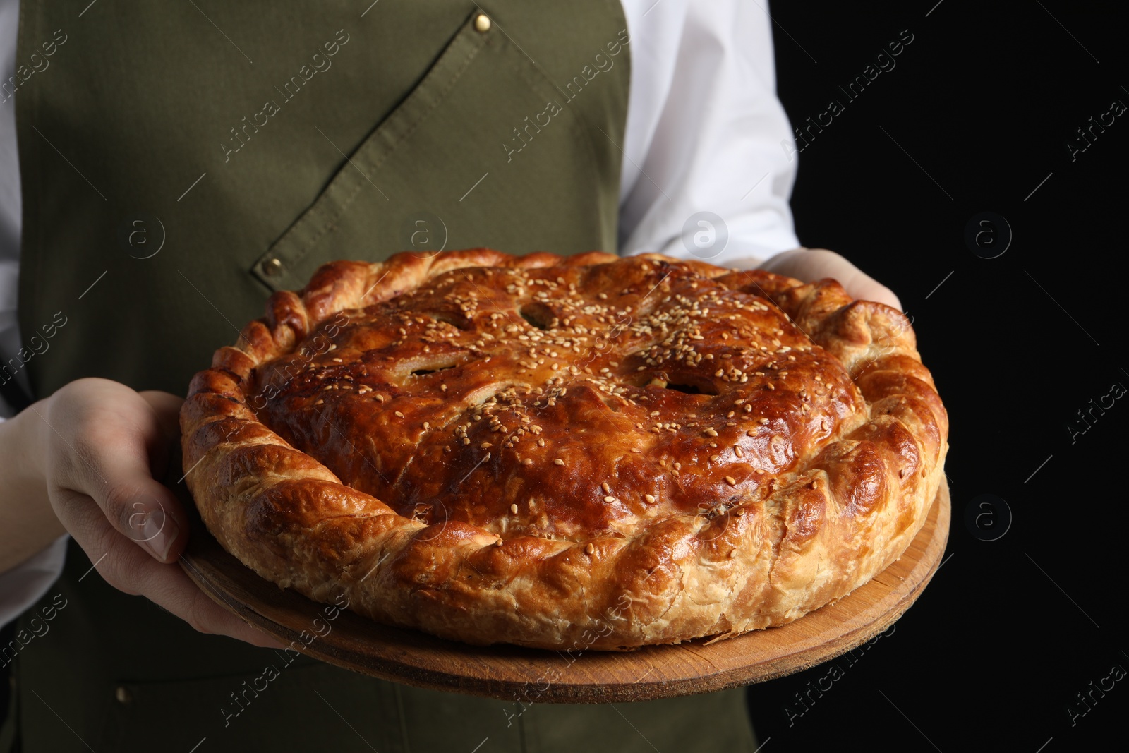 Photo of Woman holding tasty homemade pie on black background, closeup