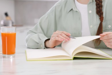 Woman writing in notebook at white marble table indoors, closeup