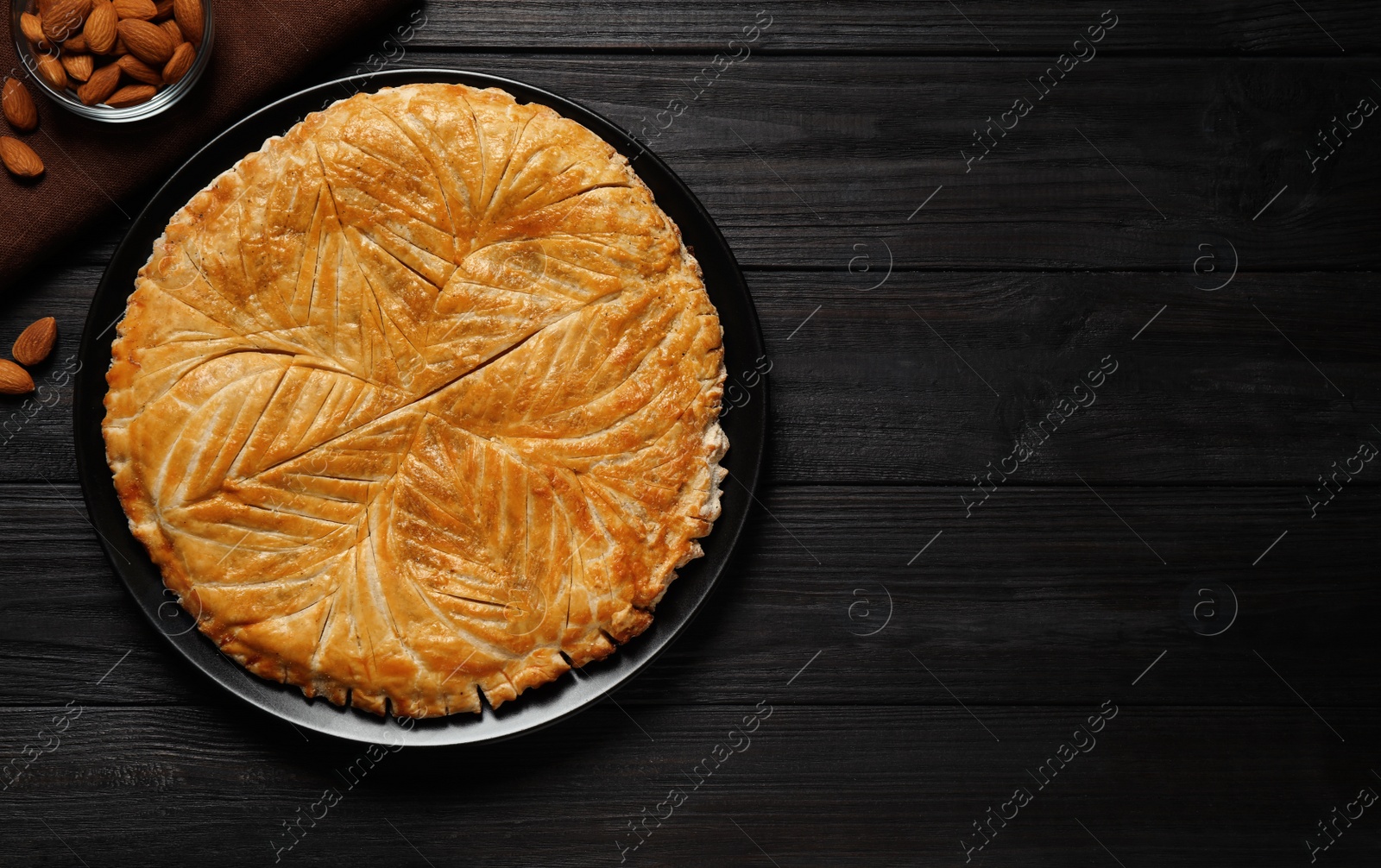 Photo of Traditional galette des rois and almonds on black wooden table, flat lay. Space for text