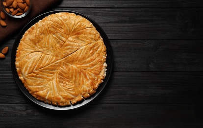 Traditional galette des rois and almonds on black wooden table, flat lay. Space for text