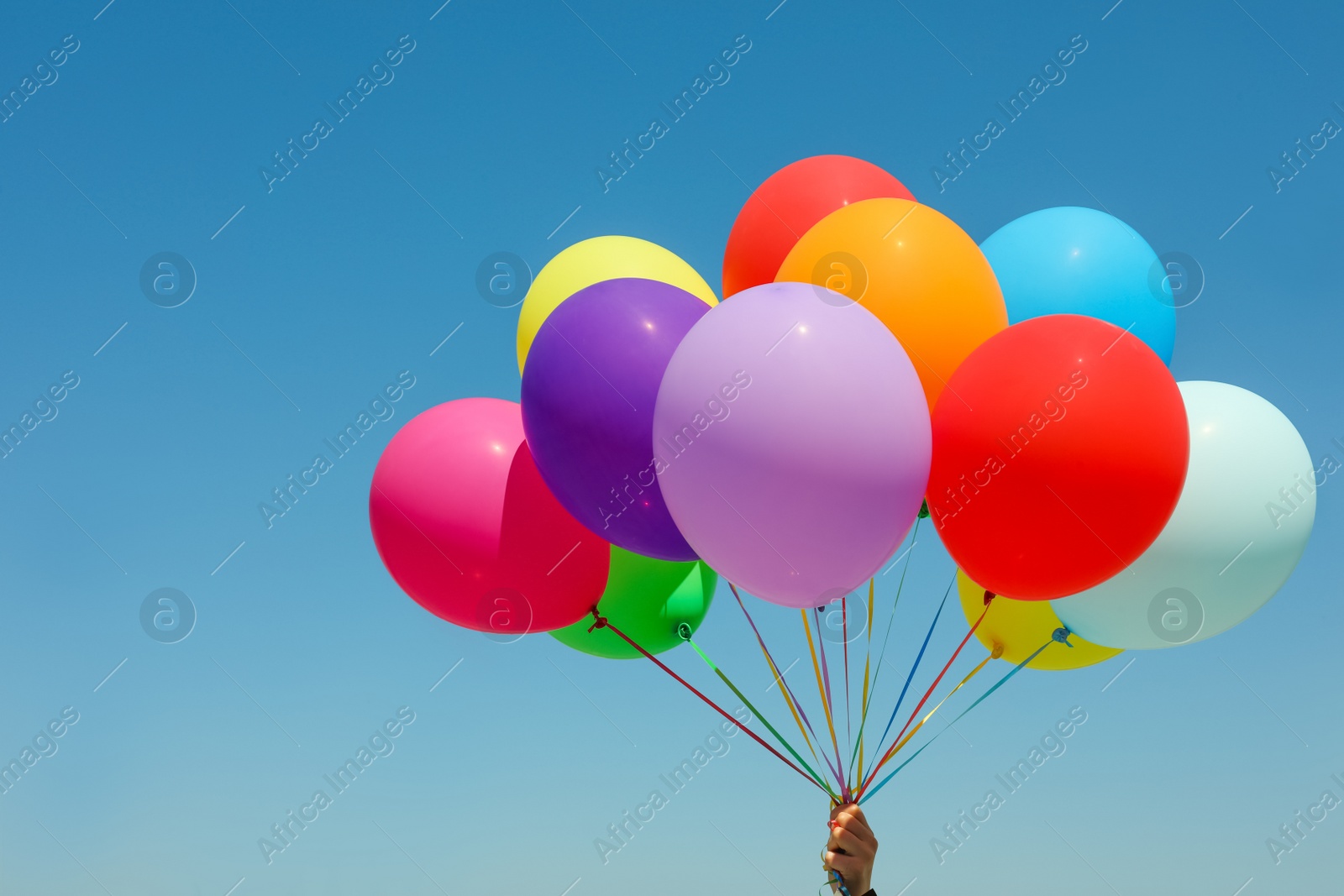 Photo of Woman with bunch of colorful balloons against blue sky, closeup