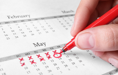 Photo of Woman marking date in calendar with red felt pen, closeup