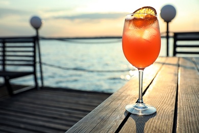 Photo of Glass of fresh summer cocktail on wooden table outdoors at sunset. Space for text