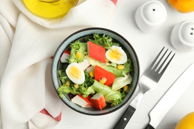Photo of Delicious salad with crab sticks and eggs in bowl on white wooden table, flat lay