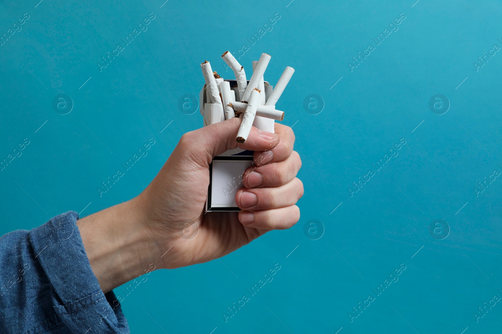 Photo of Stop smoking. Man holding pack with broken cigarettes on light blue background, closeup