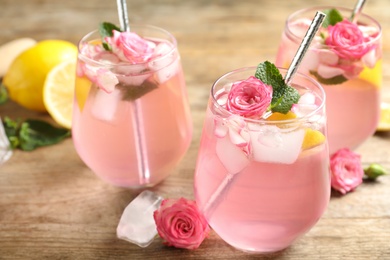 Delicious refreshing drink with rose flowers and lemon slices on wooden table, closeup