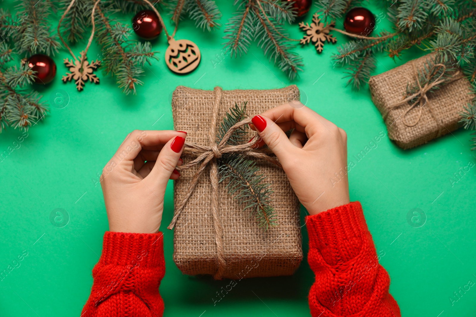 Photo of Woman with gift box near fir tree branches and Christmas decor on green background, top view