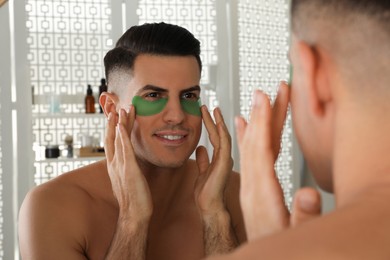 Photo of Man applying green under eye patches near mirror at home