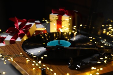 Photo of Turntable with vinyl record, fairy lights and Christmas gift boxes on grey table, closeup
