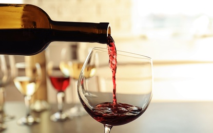 Pouring delicious red wine into glass on table