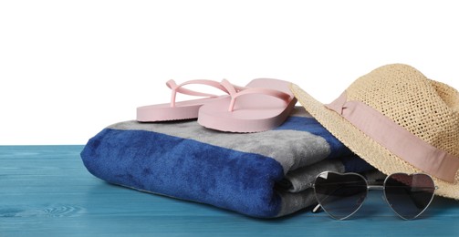 Photo of Beach towel, flip flops, hat and heart shaped sunglasses on light blue wooden surface against white background