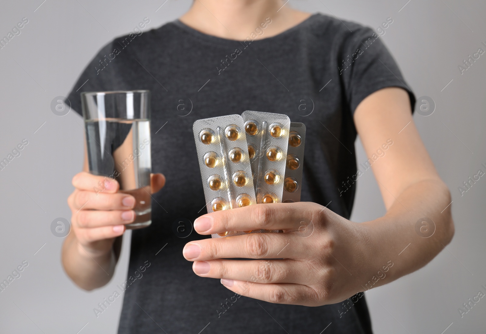 Photo of Woman holding pills in blister packs and glass of water on gray background, closeup