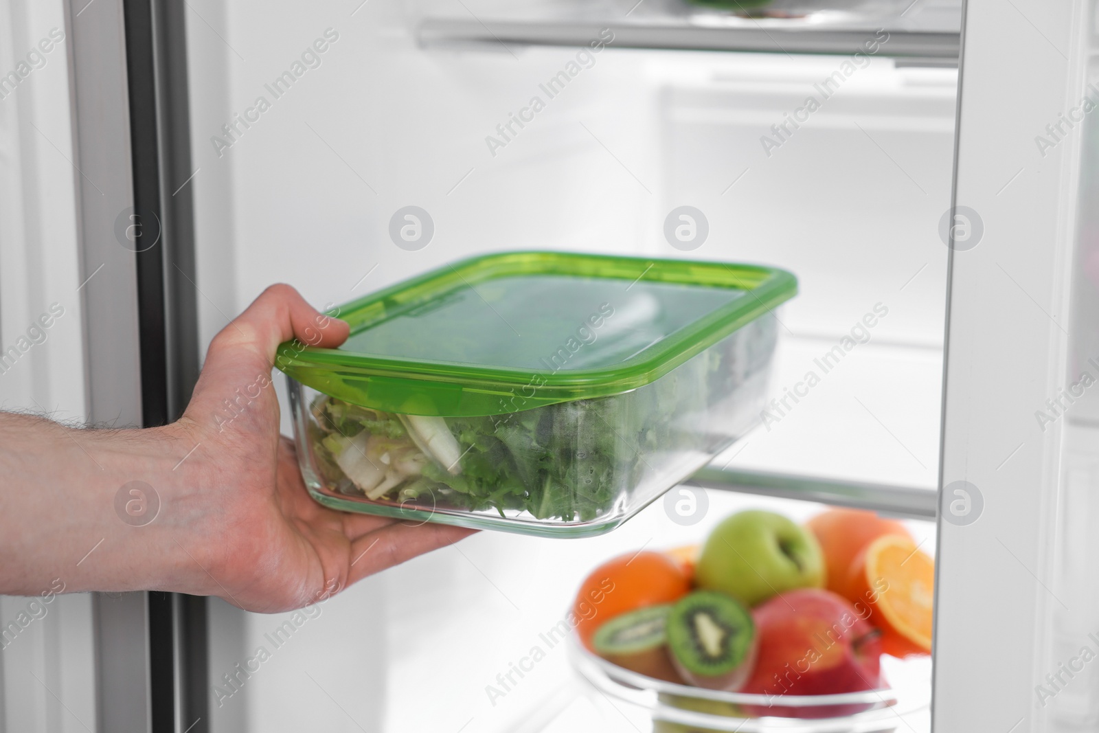 Photo of Man putting container with vegetables into refrigerator, closeup