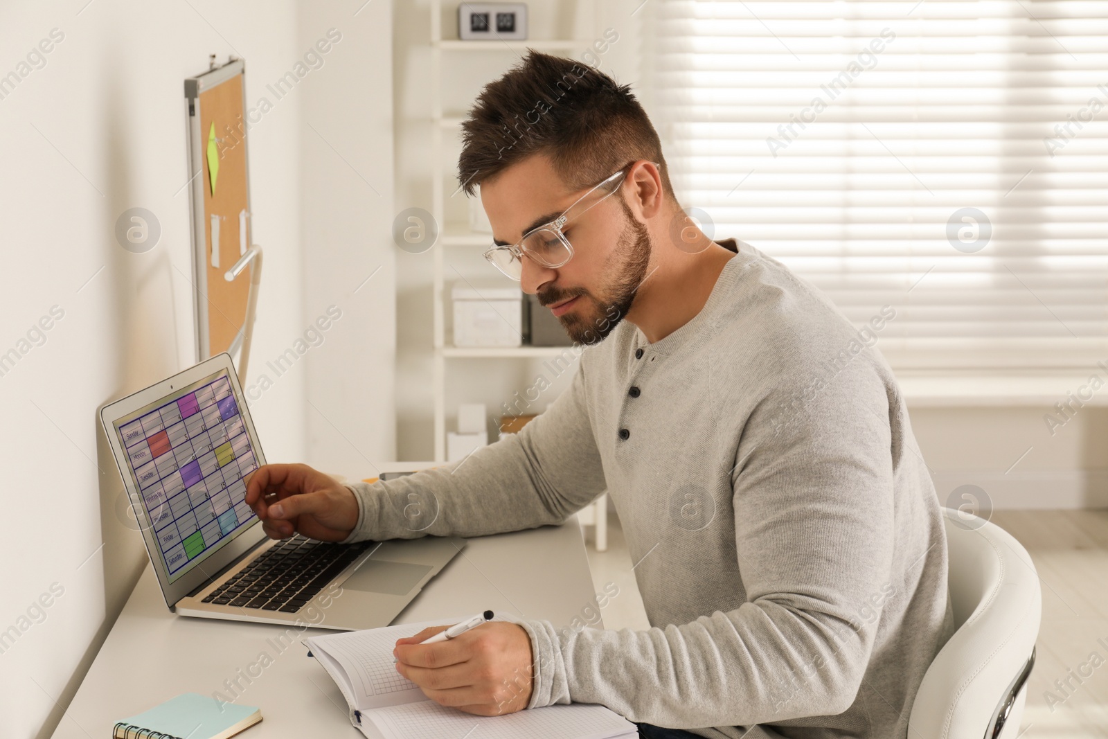 Photo of Young man using calendar app on laptop in office