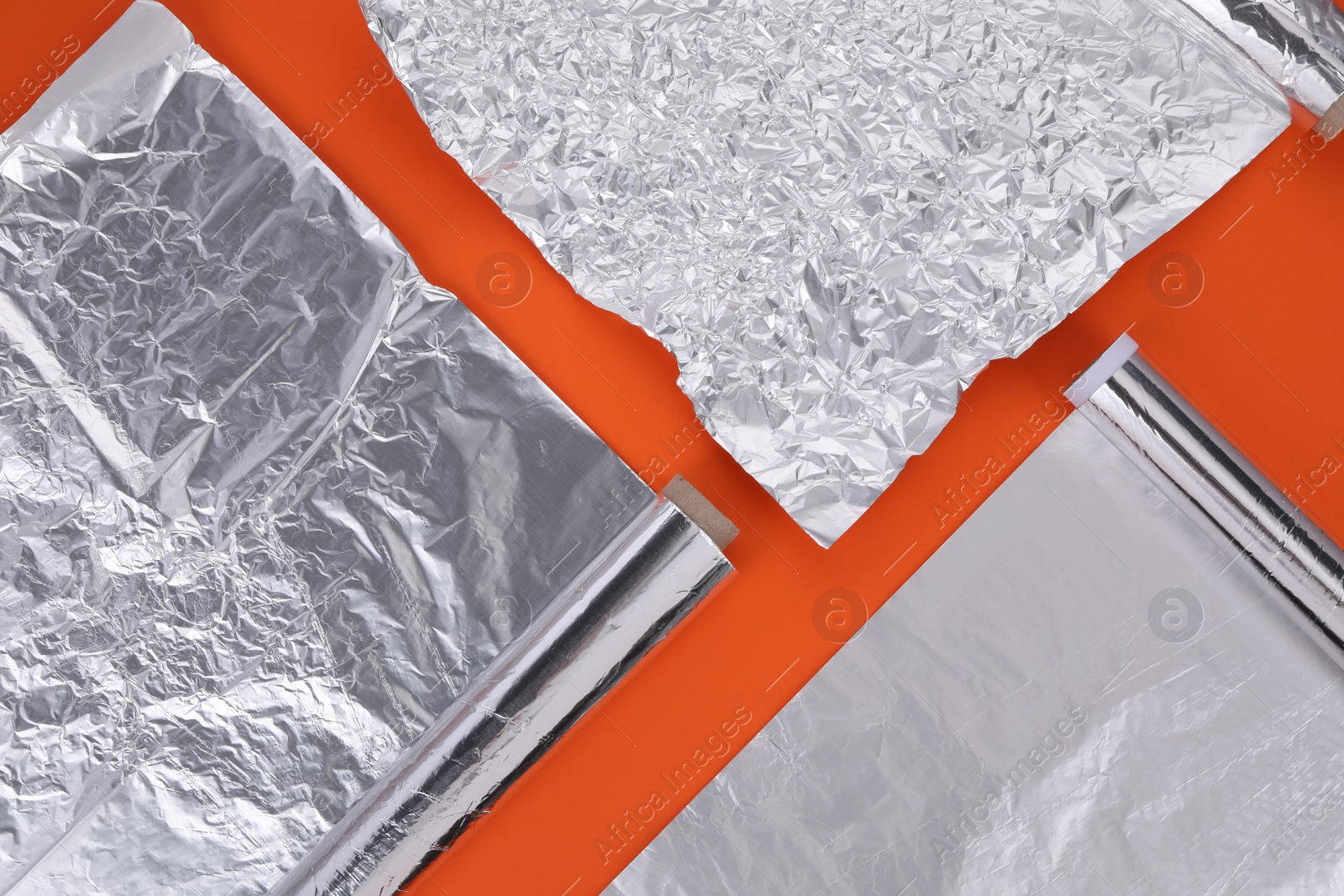 Photo of Different rolls of aluminum foil on orange background, flat lay