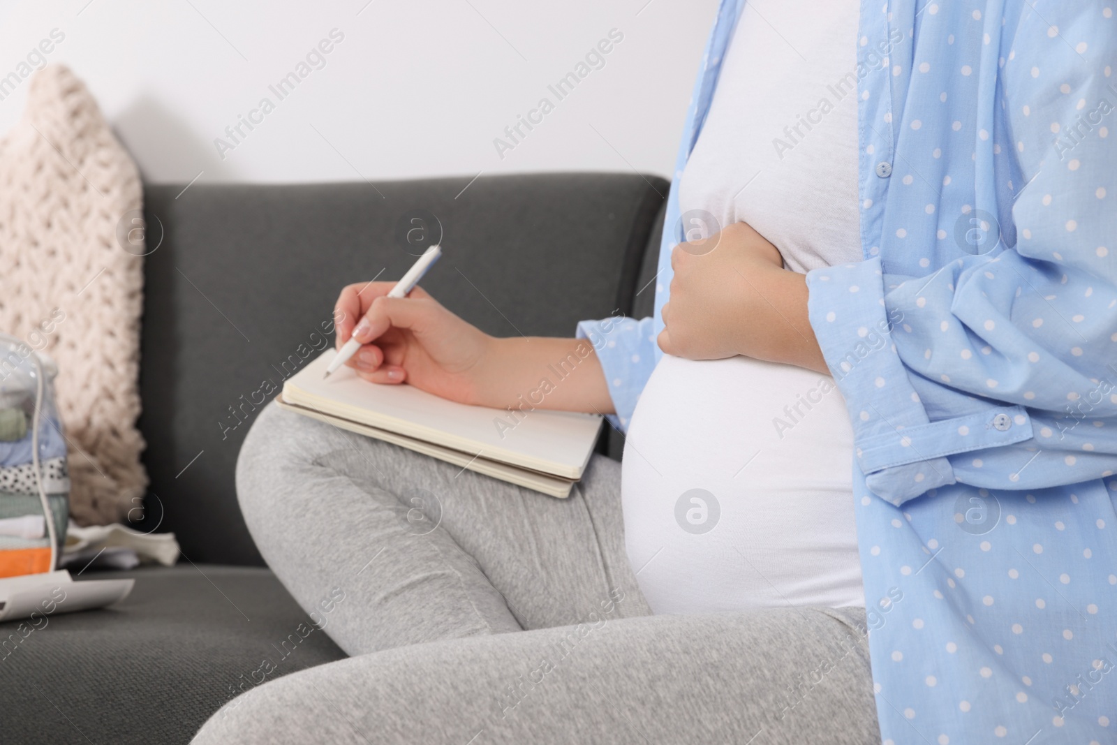 Photo of Pregnant woman preparing list of necessary items to bring into maternity hospital at home, closeup