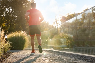 Man running outdoors on sunny day, back view. Space for text