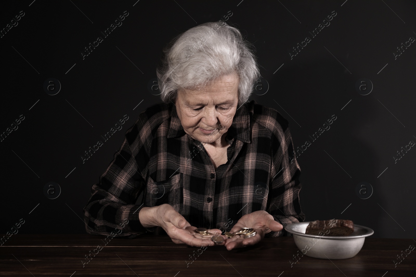 Photo of Poor mature woman with coins and bread in bowl at table