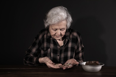 Poor mature woman with coins and bread in bowl at table