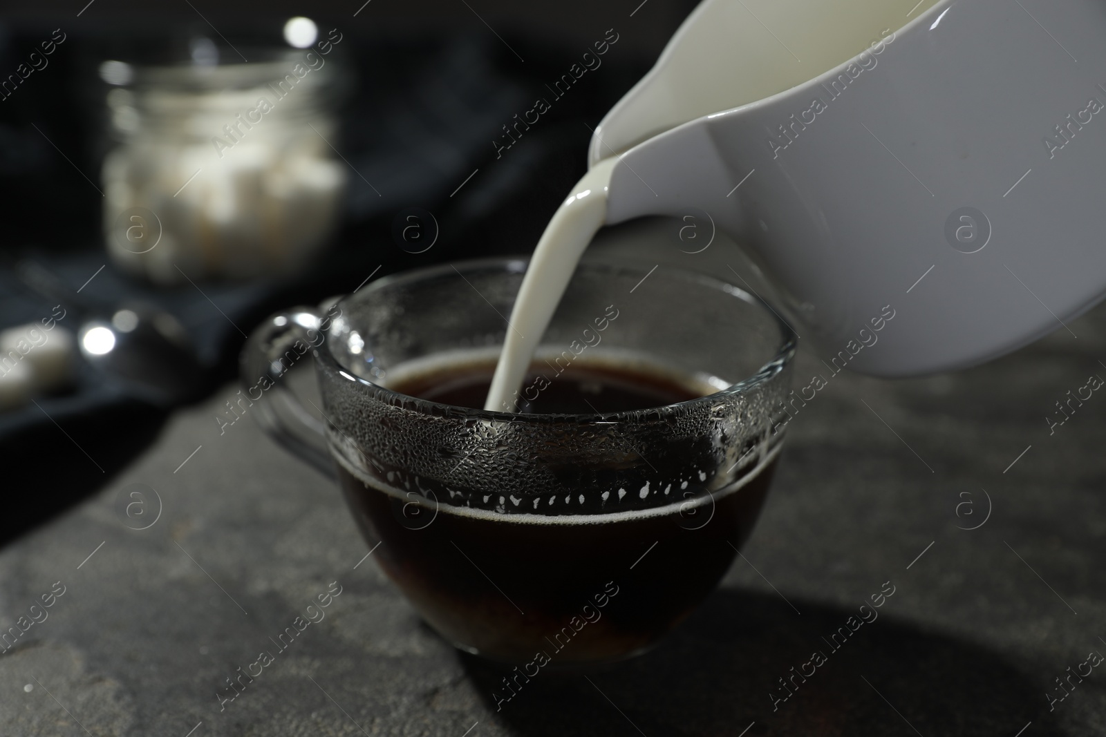 Photo of Pouring milk into cup of coffee on grey table, closeup