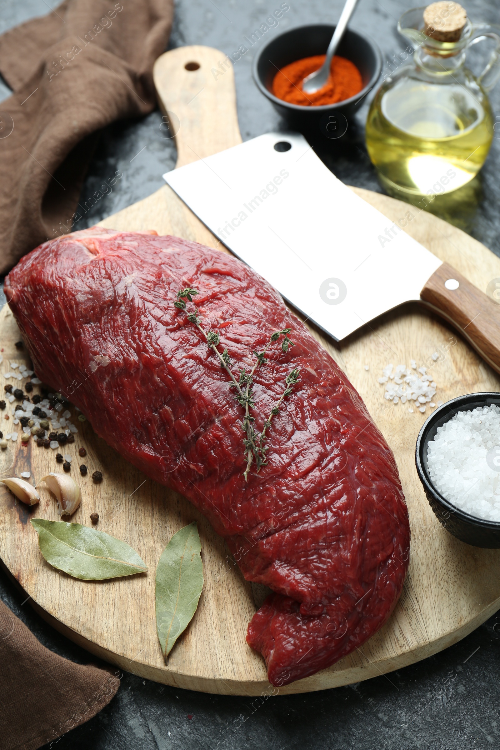 Photo of Piece of raw beef meat, knife and spices on black textured table, closeup