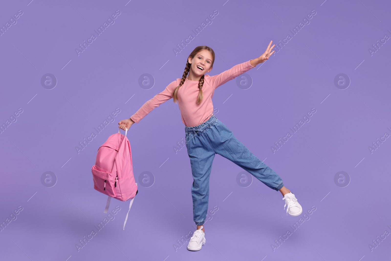 Photo of Happy schoolgirl with backpack on violet background