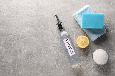 Photo of Natural cleaning products. Vinegar in bottle, baking soda, lemon, rag and sponge on grey textured table, flat lay. Space for text