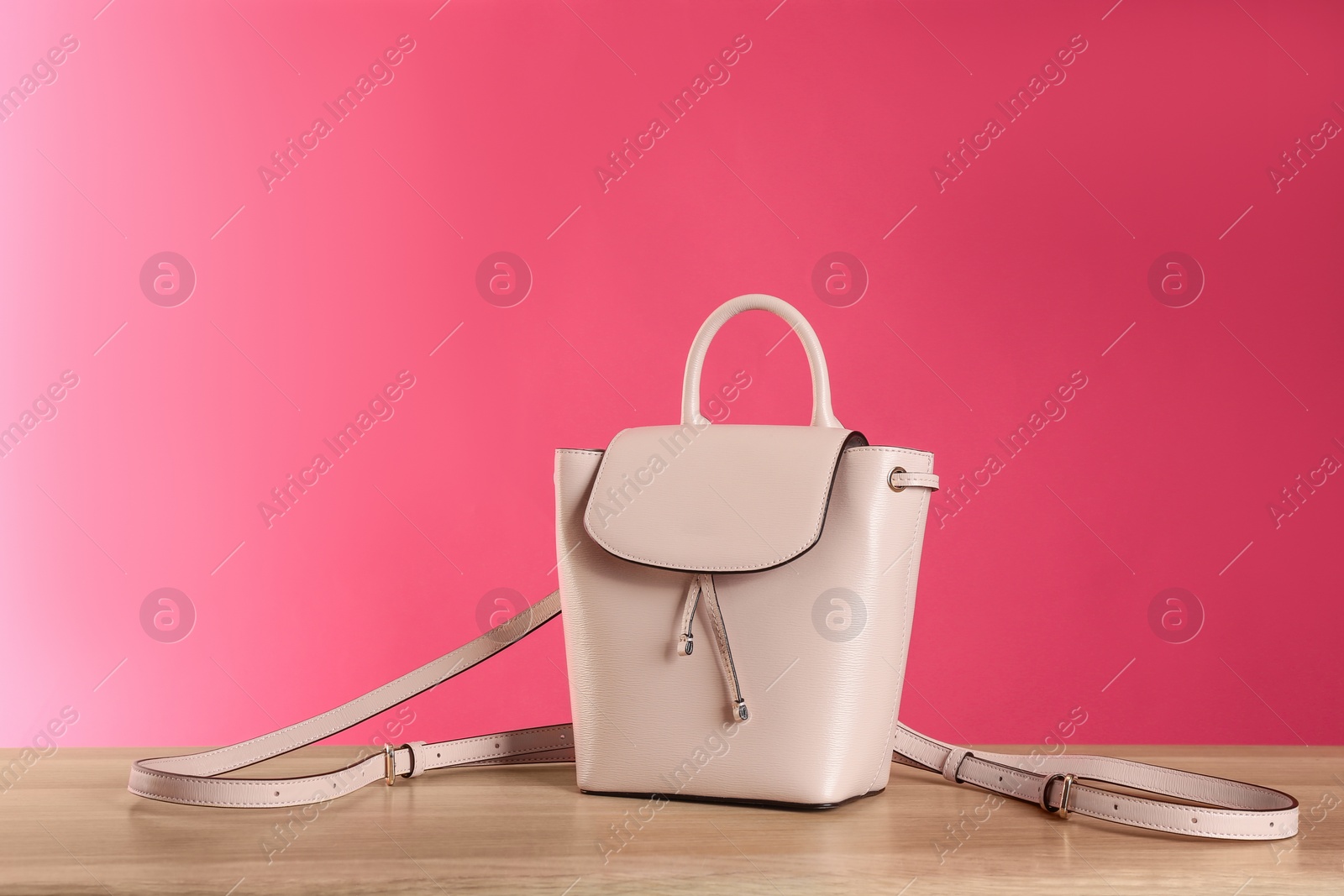 Photo of Stylish woman's bag on wooden table against pink background