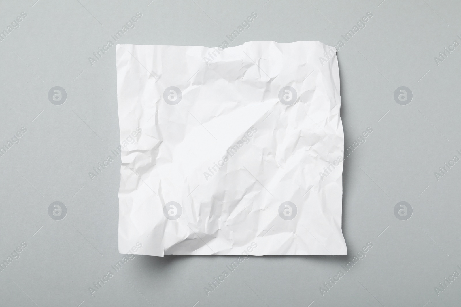 Photo of Sheet of white crumpled paper on grey background, top view