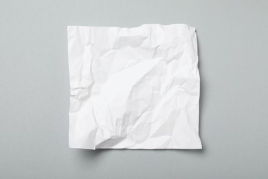 Sheet of white crumpled paper on grey background, top view