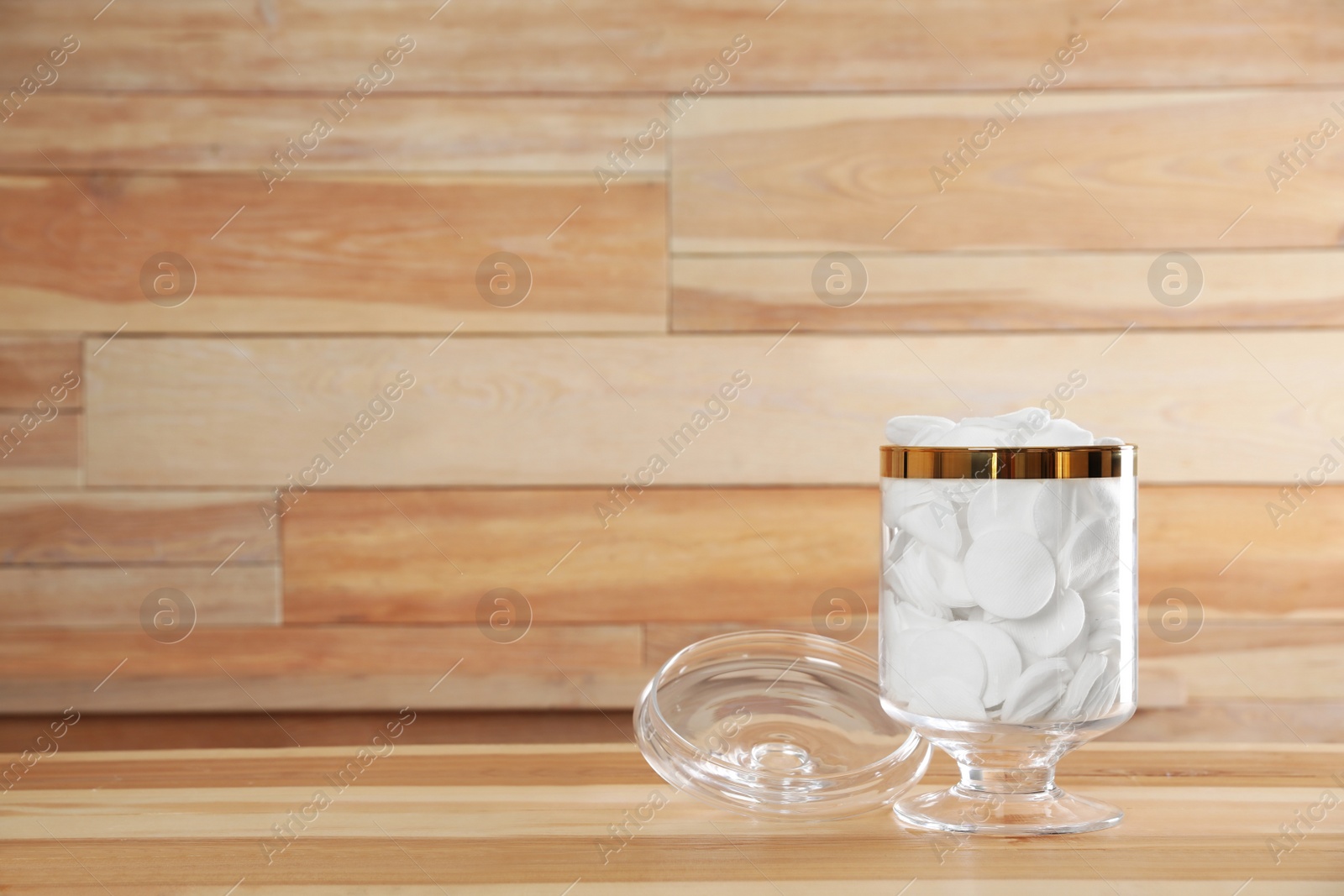 Photo of Decorative glass jar with cotton pads on table against wooden background. Space for text