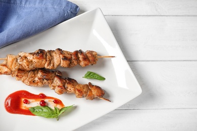 Photo of Plate with juicy shish kebab and sauce on table, top view