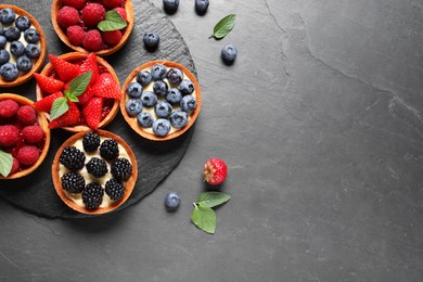 Tartlets with different fresh berries on black table, flat lay and space for text. Delicious dessert