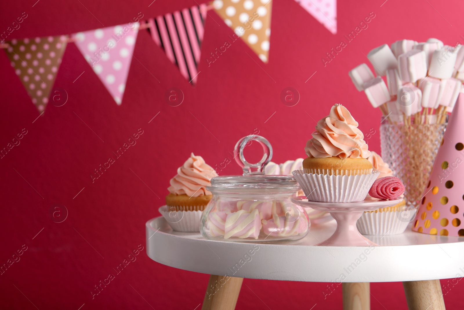Photo of Table with party hat, cupcake and other sweets on burgundy background, space for text. Candy bar