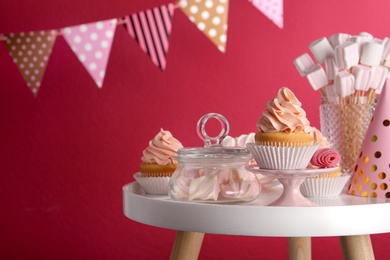 Table with party hat, cupcake and other sweets on burgundy background, space for text. Candy bar