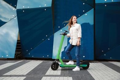 Happy woman with modern electric kick scooter on city street, space for text