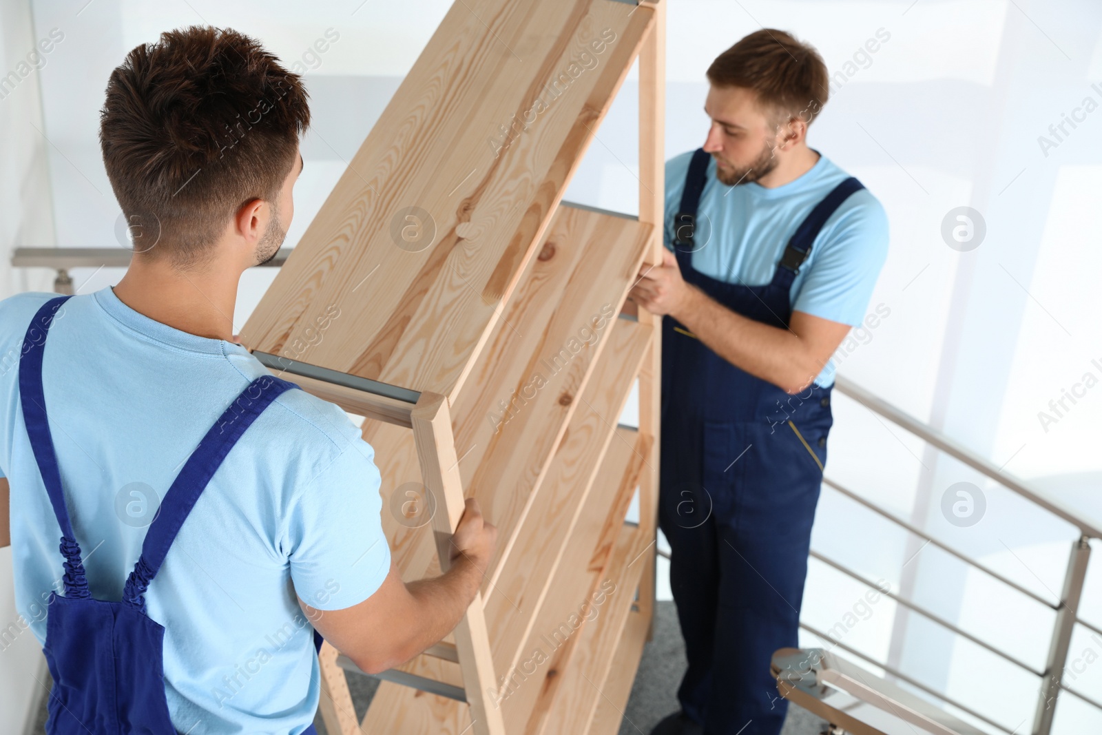 Photo of Professional workers carrying wooden rack on stairs in office. Moving service