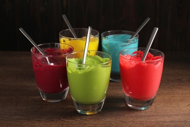 Glasses of different cream with food coloring on wooden table