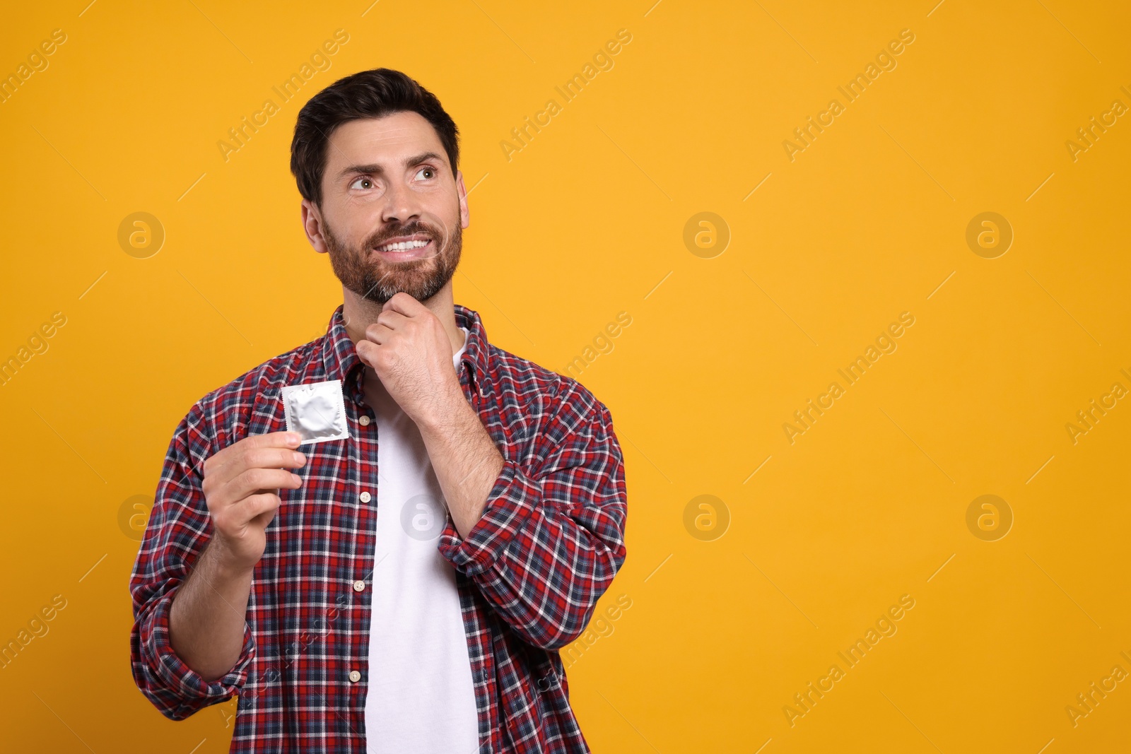 Photo of Happy man holding condom on yellow background, space for text. Safe sex