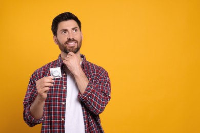Happy man holding condom on yellow background, space for text. Safe sex
