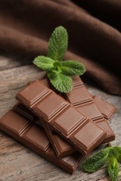 Tasty milk chocolate pieces with mint on wooden table, closeup