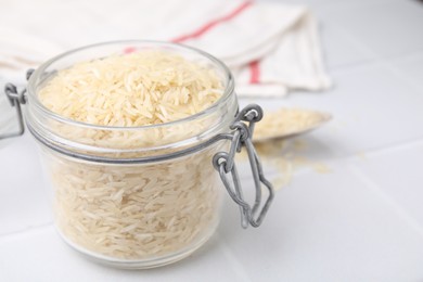 Photo of Raw rice in glass jar on white table, closeup. Space for text