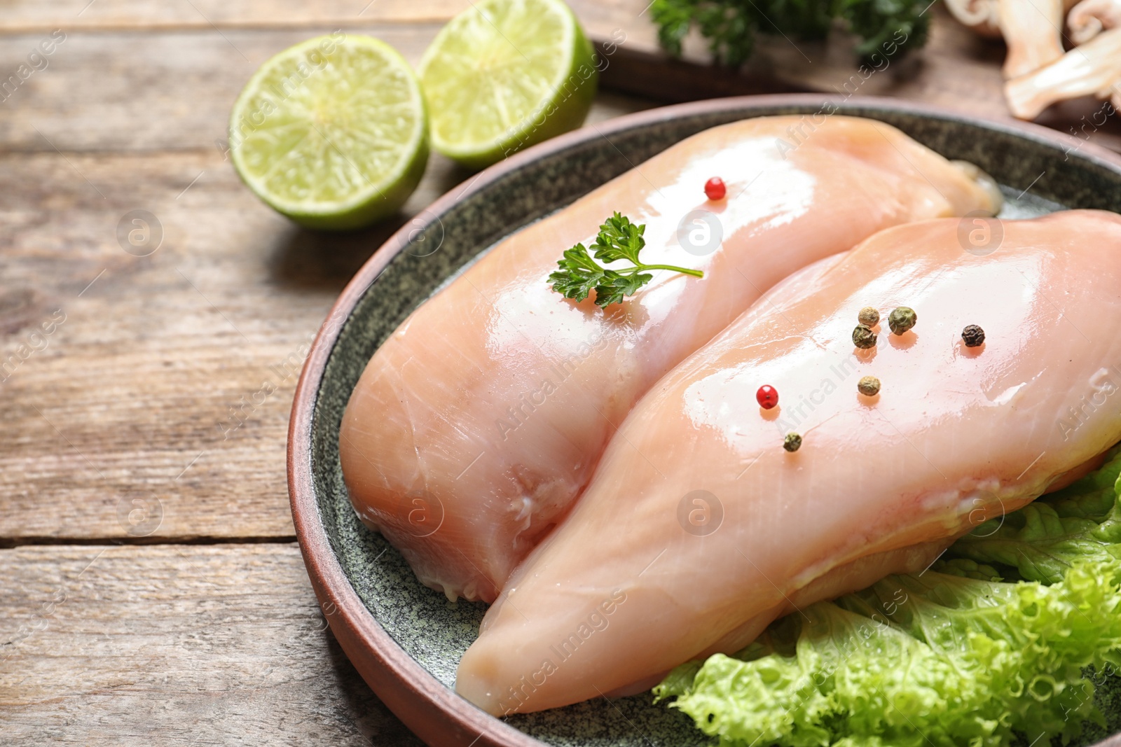 Photo of Plate with raw chicken breasts and ingredients on wooden table