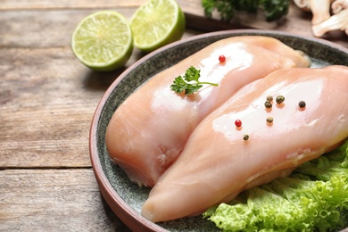 Plate with raw chicken breasts and ingredients on wooden table