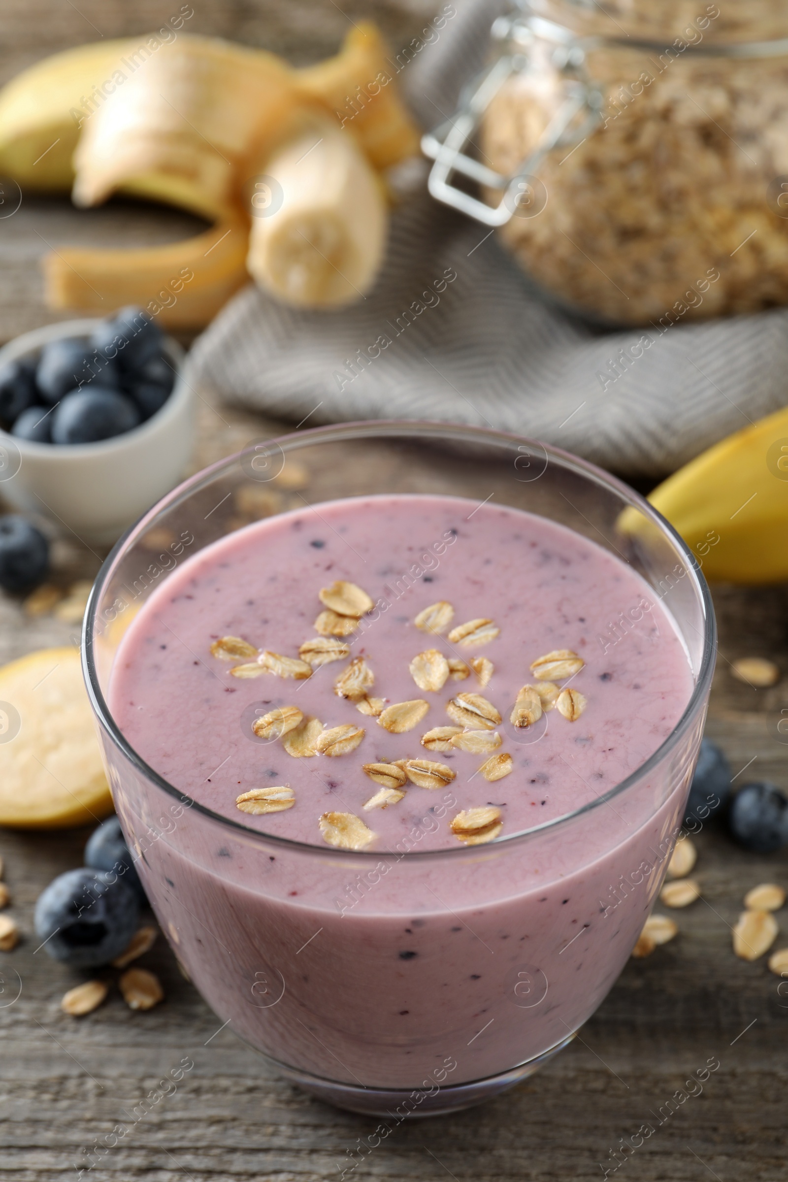 Photo of Glass of tasty banana blueberry smoothie with oatmeal on wooden table