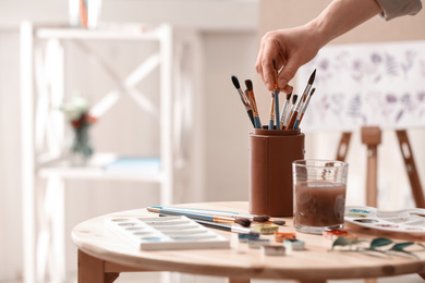 Photo of Watercolorist taking brush from holder on table in workshop, closeup