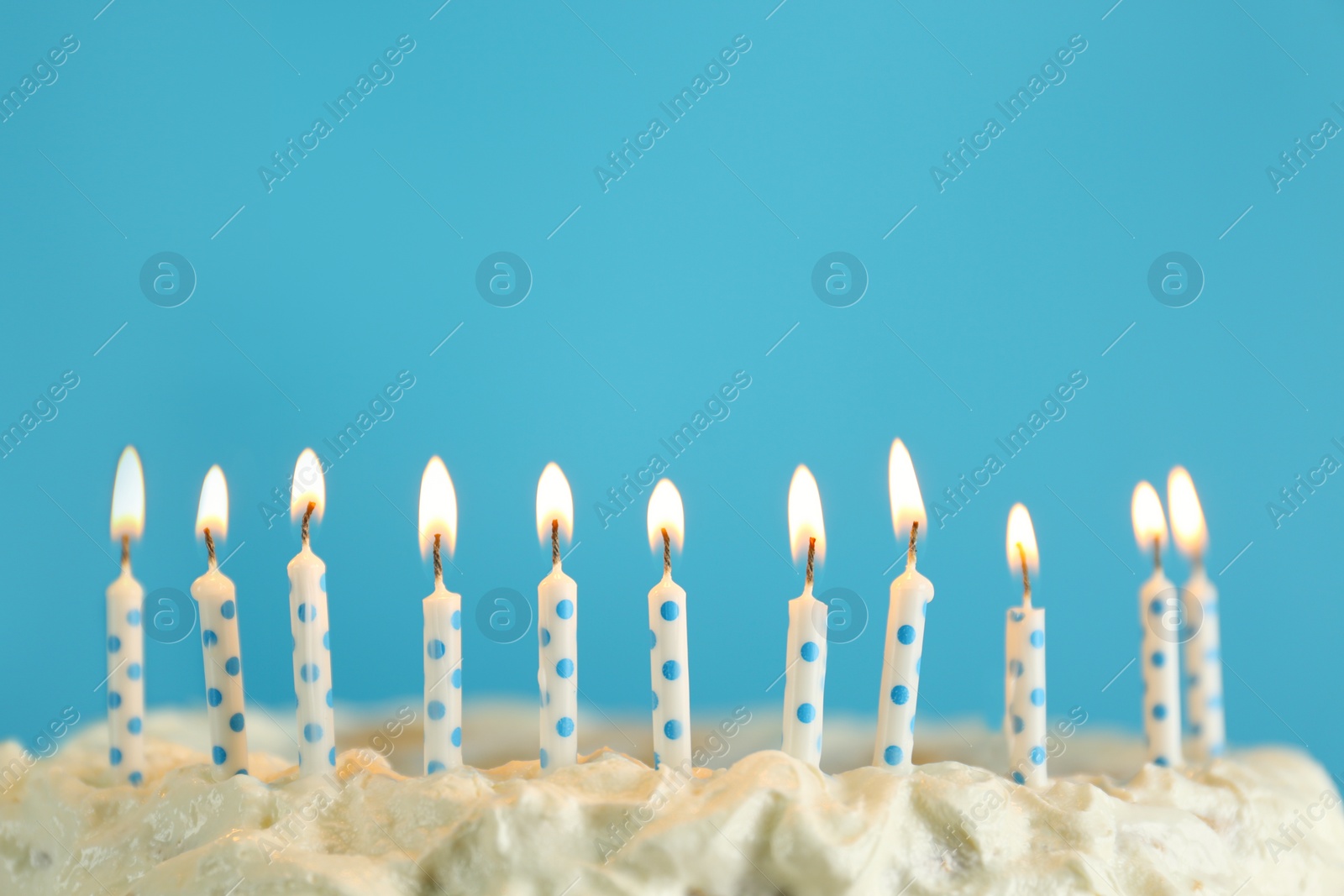 Photo of Birthday cake with burning candles on light blue background, closeup