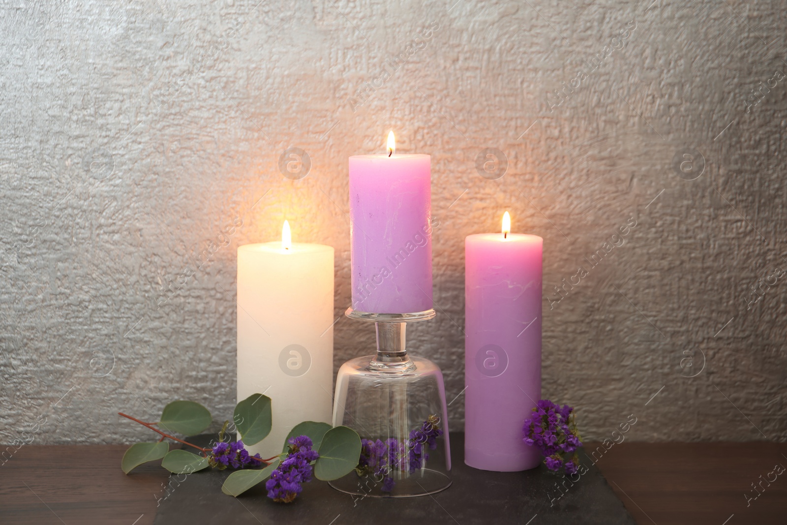 Photo of Candles with floral decor on table against color background