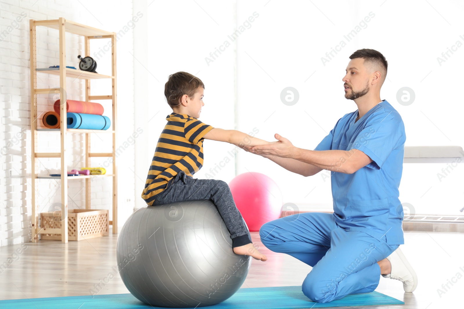 Photo of Orthopedist working with little boy in hospital gym