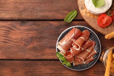 Photo of Rolled slices of delicious jamon and different products on wooden table, flat lay. Space for text